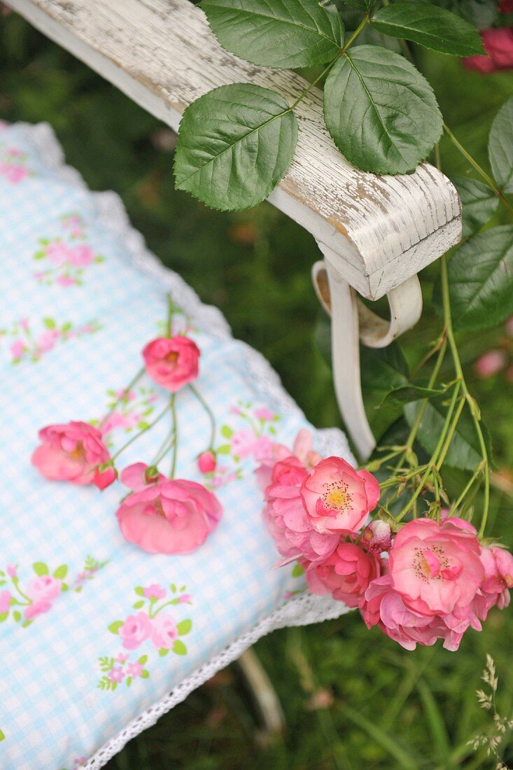 Detail of chair with arm rest and sprays of shrub roses lying on patterned cushion