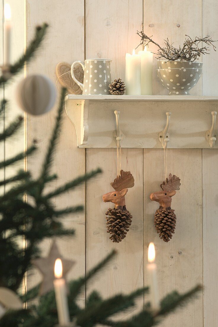 Wooden pine cones with moose heads hanging from coat rack with crockery and candles on shelf above
