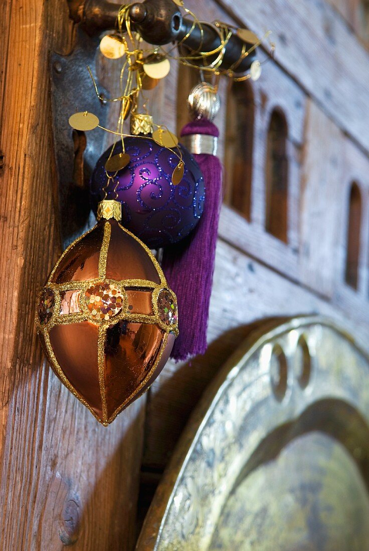 Exotic Christmas arrangement of copper-coloured pendant and purple bauble and tassel hanging on wrought iron door handle