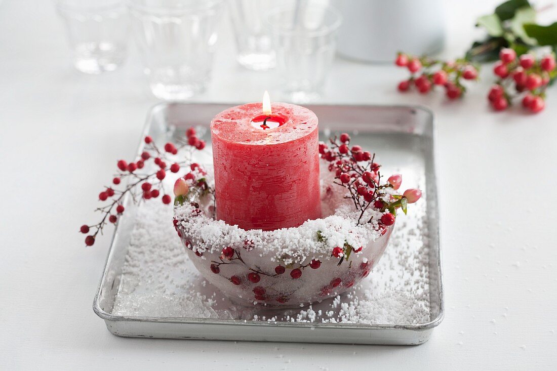 Red candle in ice bowl with St. John's wort berries, Skimmia japonica berries and artificial snow