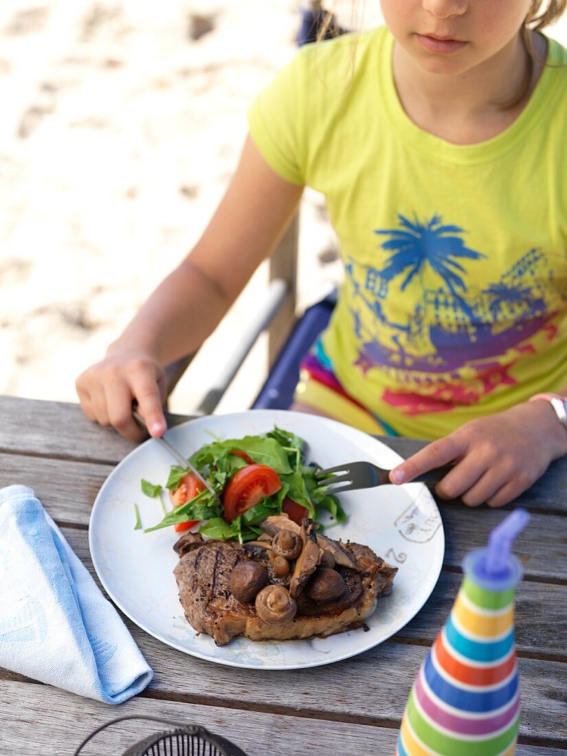 A girl eating a grilled steak with mushrooms