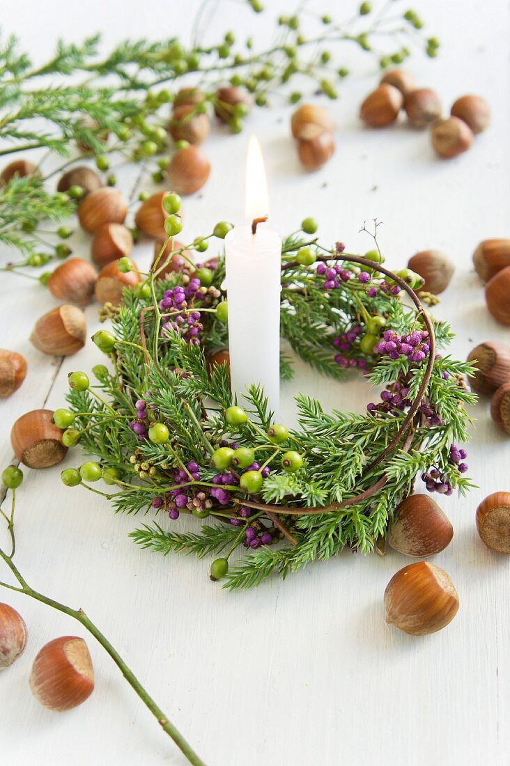 Haselnüsse und Kerze mit Kranz aus Callicarpa und Koniferen