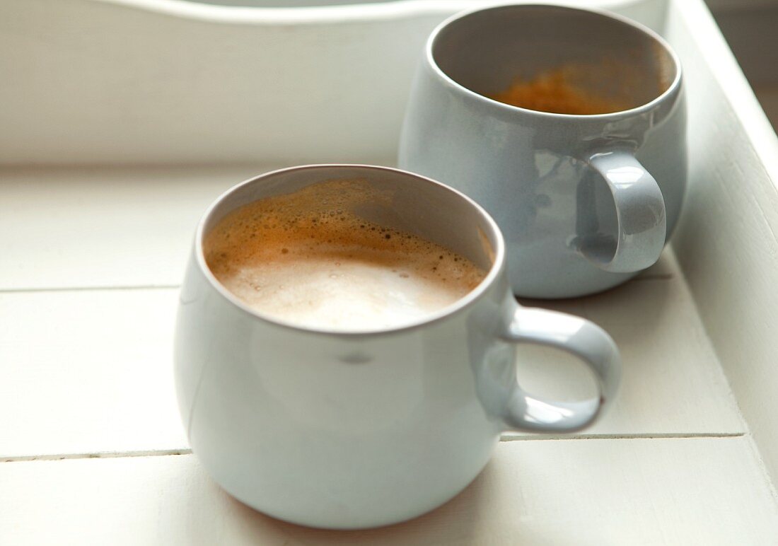 Zwei Becher mit Cappuccino auf Holztablett