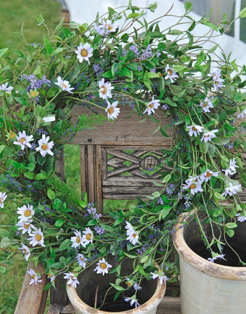 Blumenkranz mit Margeriten und Tontöpfe auf einem Holzstuhl