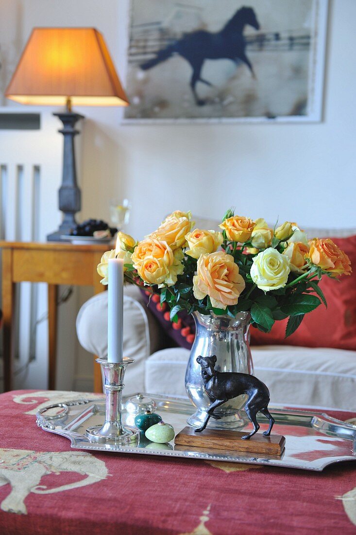 Tray with silver vase of roses and lit candle on coffee table in traditional living room