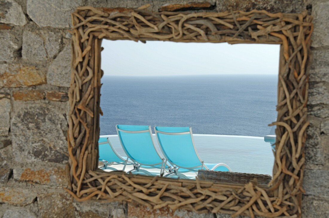 Mirror with frame made of twigs reflecting deckchairs and the sea