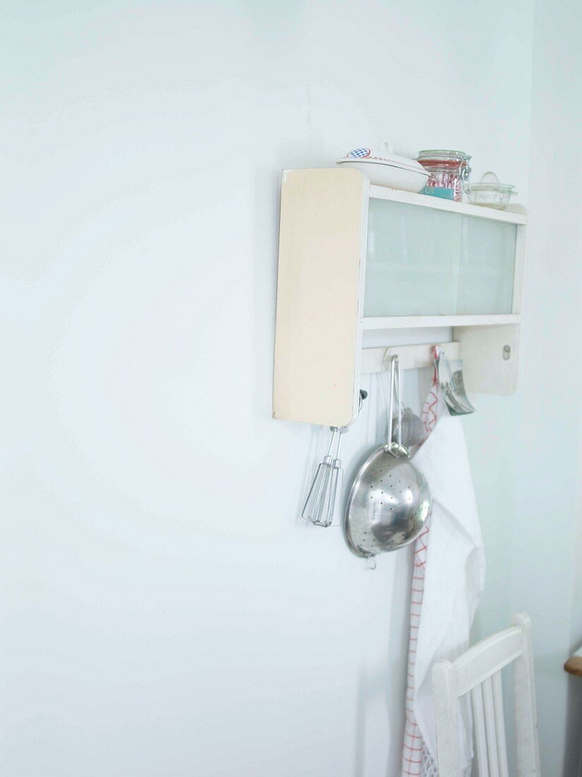 Detail of simple kitchen with kitchen utensils hanging from wall-mounted cabinet