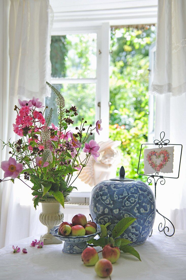 Blue and white glazed china pot with lid and bouquet on table in front of window with view of garden