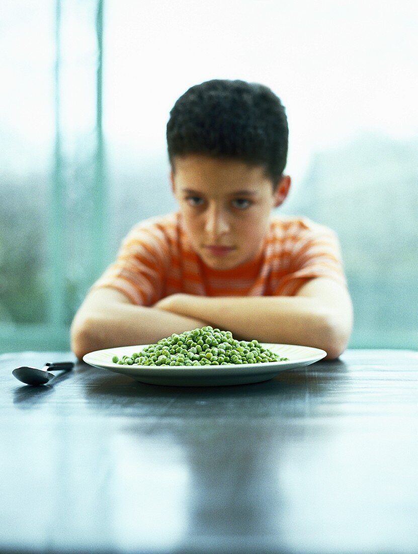 A boy sitting in front of a plate of peas
