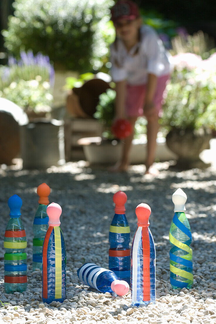 Kind spielt Kegelspiel mit bunten Flaschen im Kiesgarten