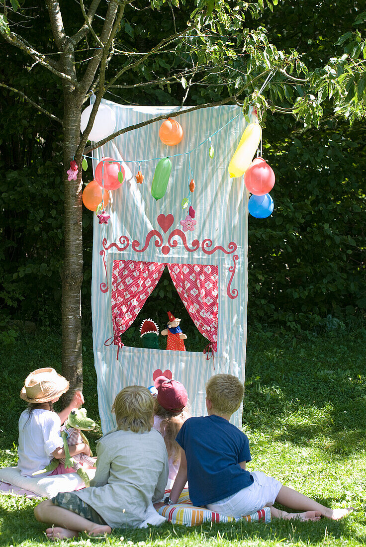 DIY-Kaspertheater aus Stoff, Kinder, Ballons und Garten bei Sonnenschein