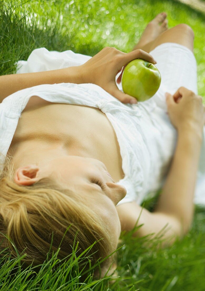 Junge Frau mit Apfel liegt auf der Wiese