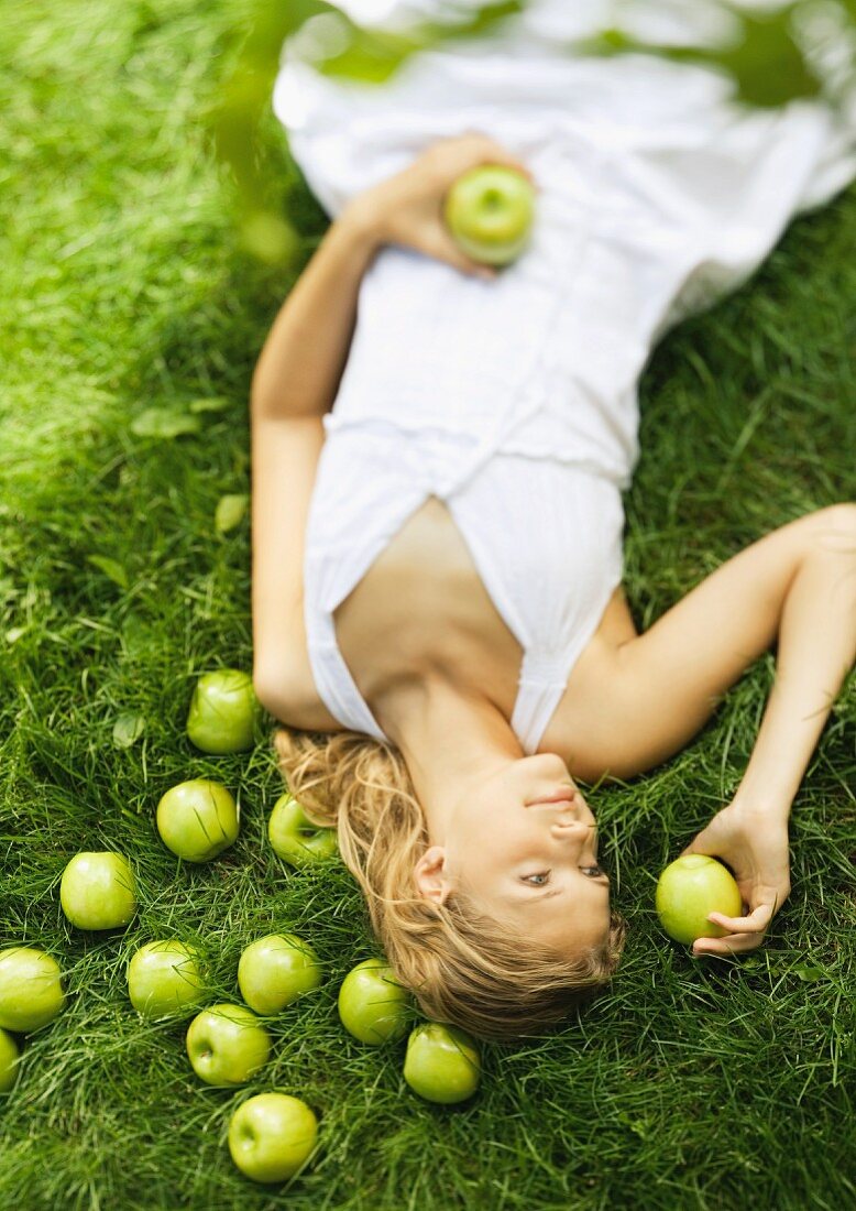 Junge Frau liegt auf der Wiese mit Äpfeln