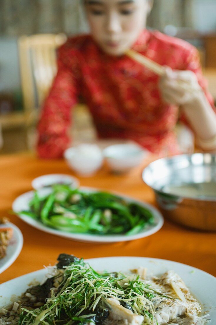 Young woman wearing traditional Chinese clothing, eating with chopsticks, focus on food in foreground