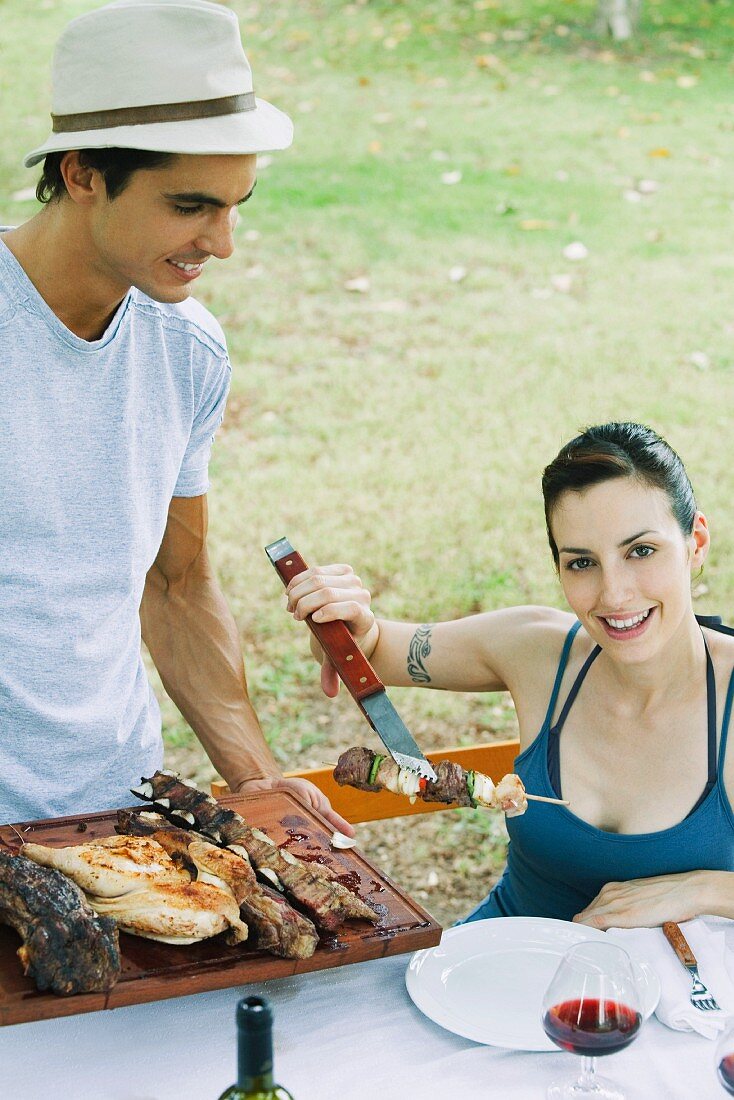 Woman taking kebab from tray of grilled meats, smiling at camera