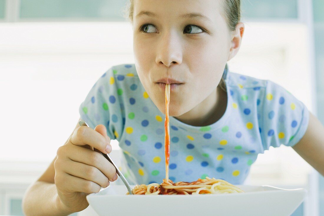 Girl eating spaghetti with tomato sauce