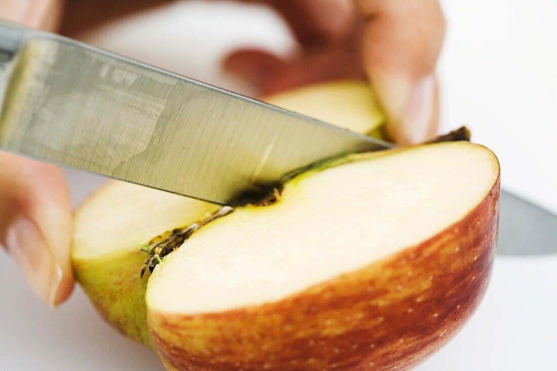 Woman cutting apple with knife, close-up, cropped view of hand