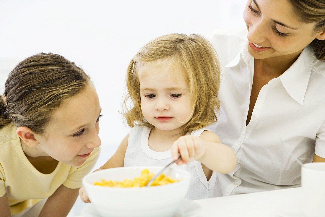 Kleines Mädchen isst Cornflakes, Mutter und Schwester schauen zu