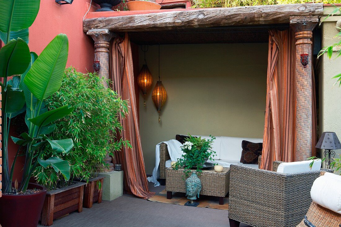 Moderne Outdoormöbel aus Rattan und tropische Pflanzen im Kübel neben mediterraner Loggia mit Sofa