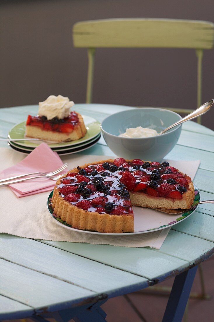 Erdbeer-Heidelbeer-Kuchen mit Sahne auf Gartentisch