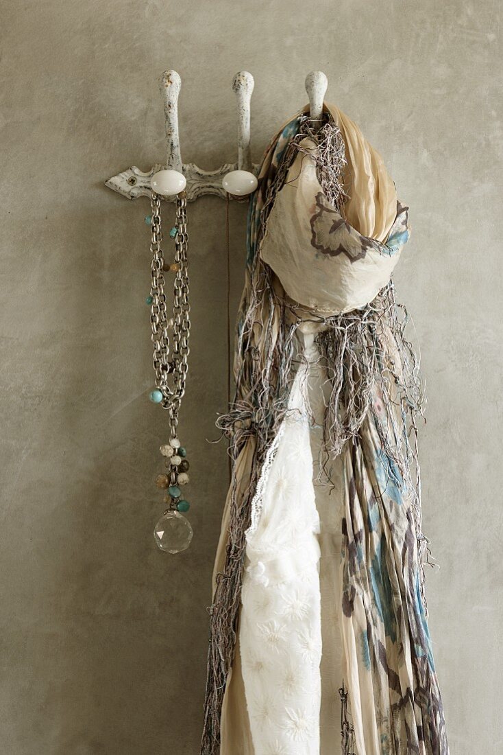 Fringed scarf and necklace hanging from clothes pegs on concrete wall