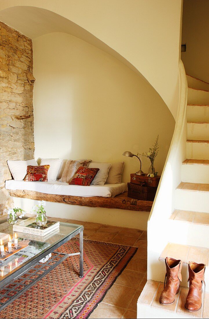 Modern coffee table in front of masonry bench next to winding staircase with boots on bottom tread