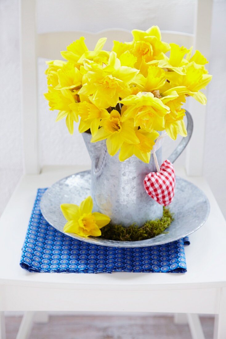 Bouquet of narcissus in zinc pitcher with moss wreath and small fabric heart