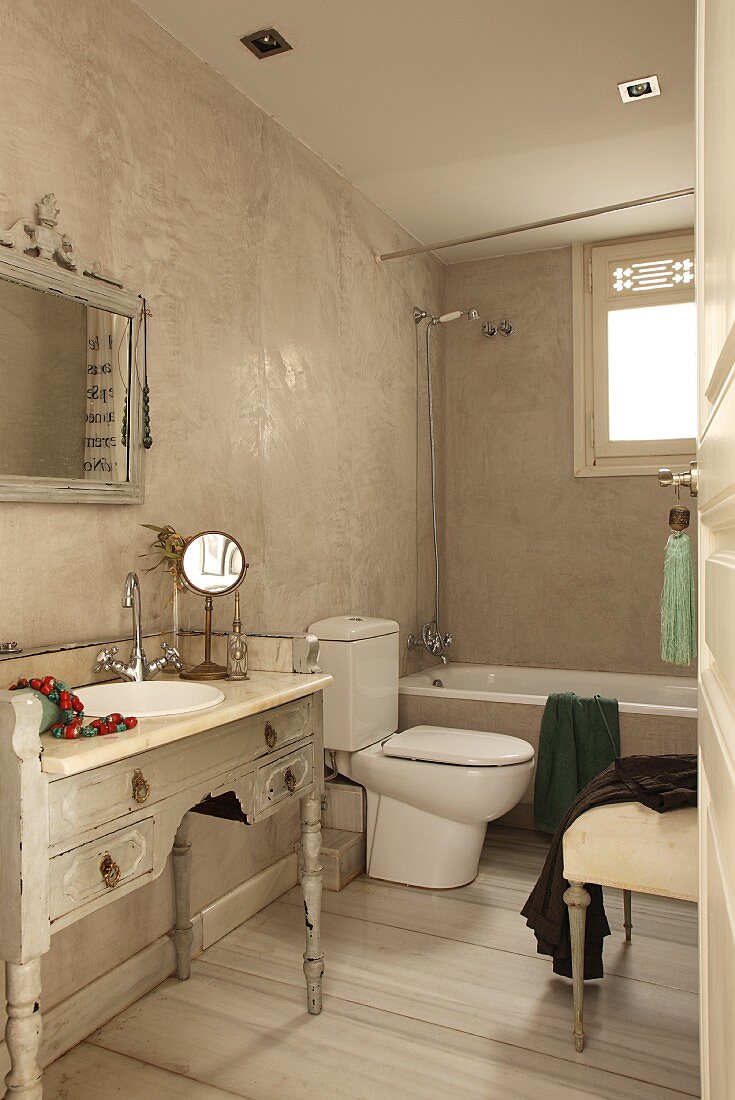 Vintage-Bad mit antikem Schminkmöbel als Waschtisch für das Einbaubecken; modernes WC im Kontrast zu Wänden in heller Marmor-Spachteltechnik