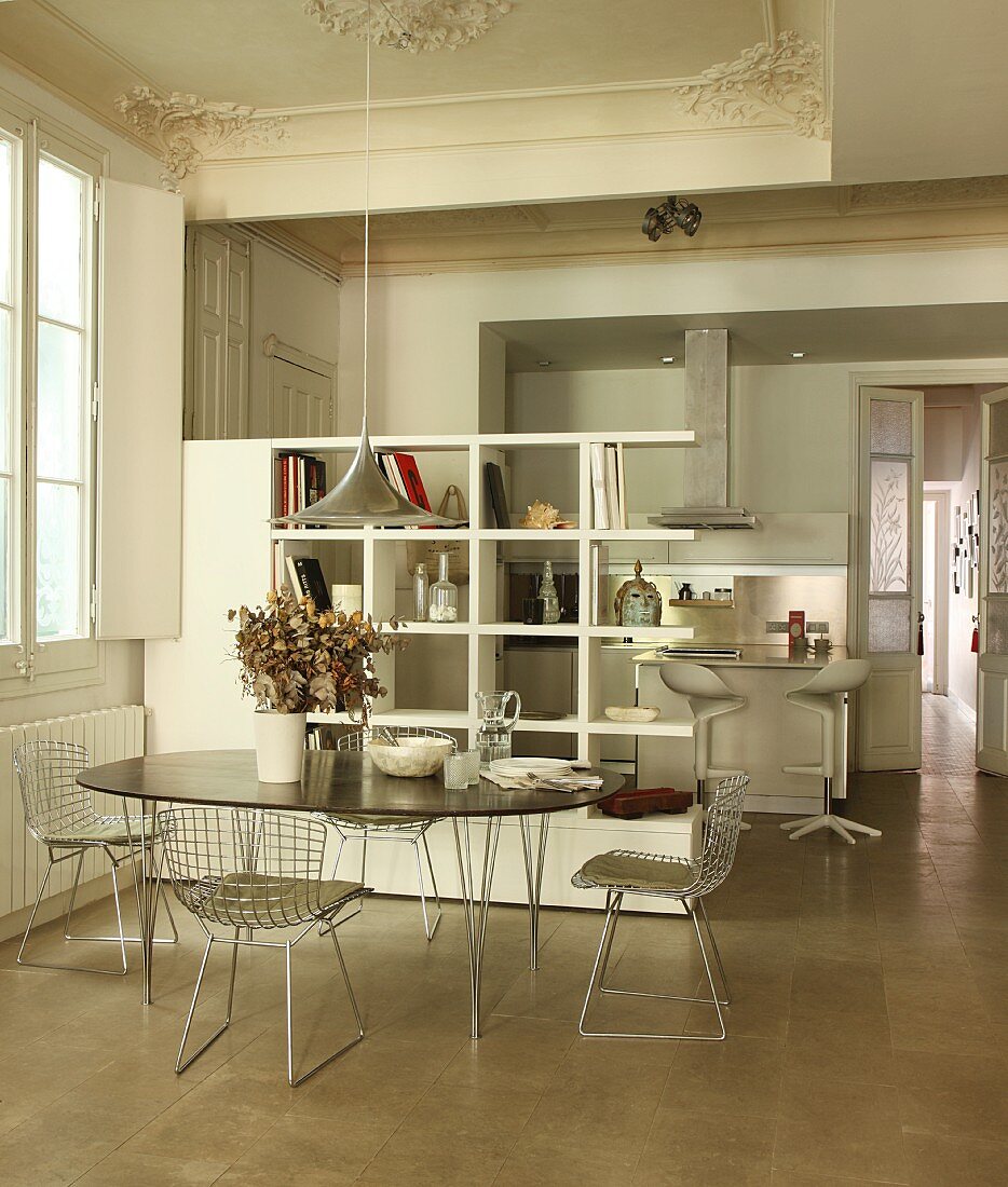 Esstisch mit Designklassikern der 50er und 60er Jahre in stilvoller Altbauwohnung mit Stuckdecken; Regalraumteiler zur modernen, offenen Küche