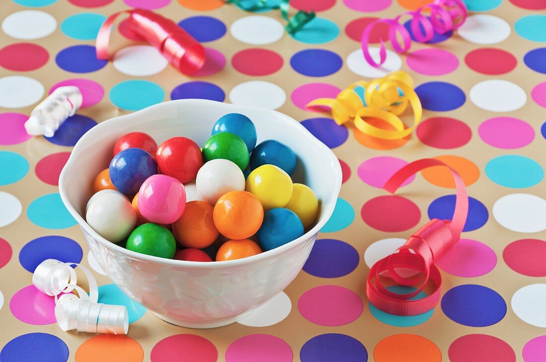 A Bowl of Colorful Gumballs on a Polk-a-Dot Table Cloth with Scattered Party Ribbons