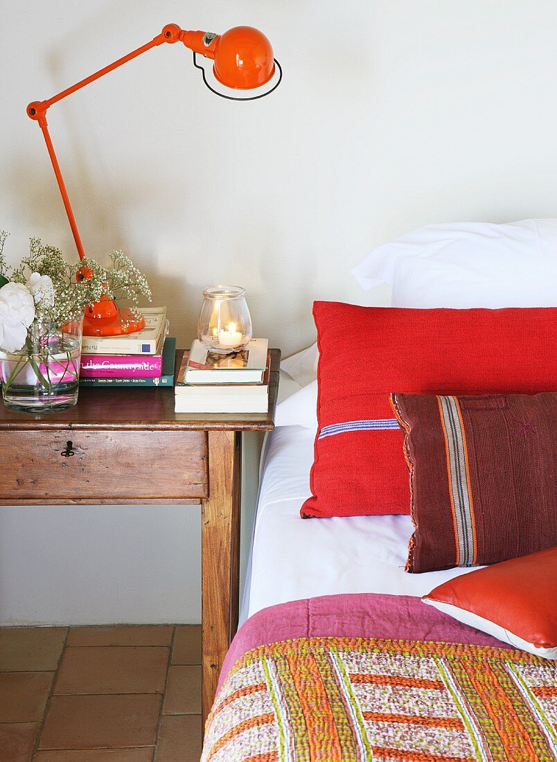 Red retro table lamp on bedside table next to bed with red scatter cushions and bedspread