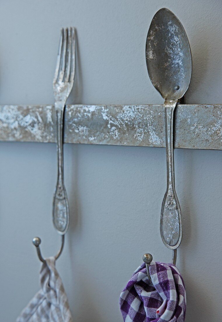 Rusty hook rail with cutlery motif and partial view of tea towels hanging from hooks