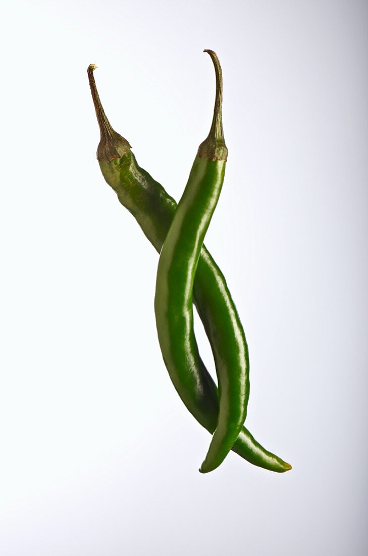 Two green chilli peppers against a white background