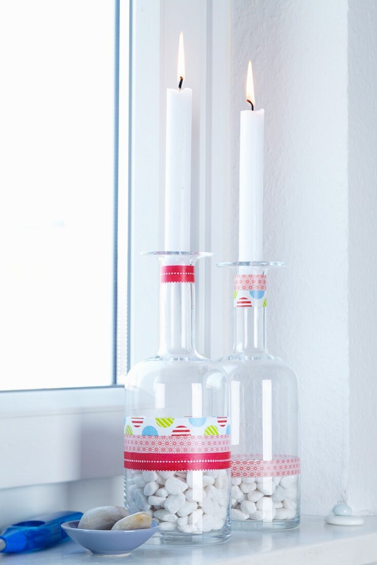 Brennende Kerzen auf Glasflaschen mit Kieselsteinen und bunten Masking Tape Streifen als Badezimmerdeko