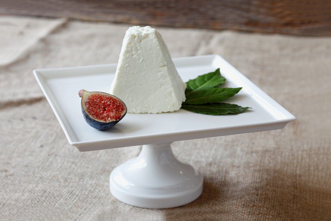 Sheep Cheese with Fig and Bay Leaves on a White Pedestal Dish