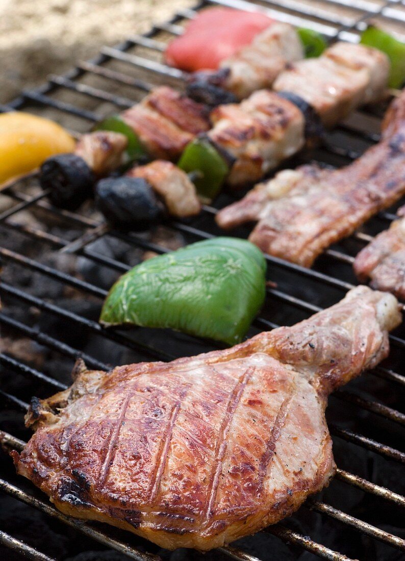 A pork chop, bacon and kebabs on a barbecue