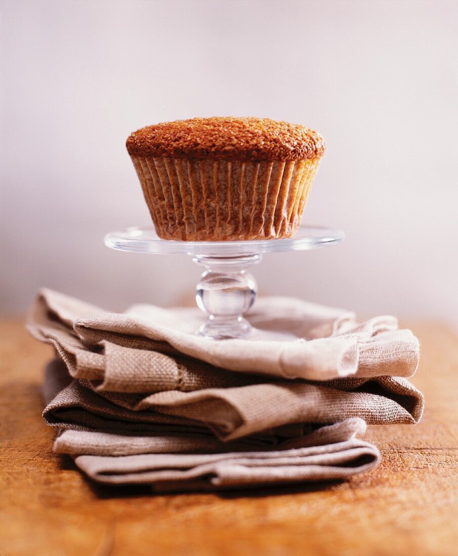 A Single Bran Muffin on a Small Pedestal Dish on Stacked Cloth Napkins