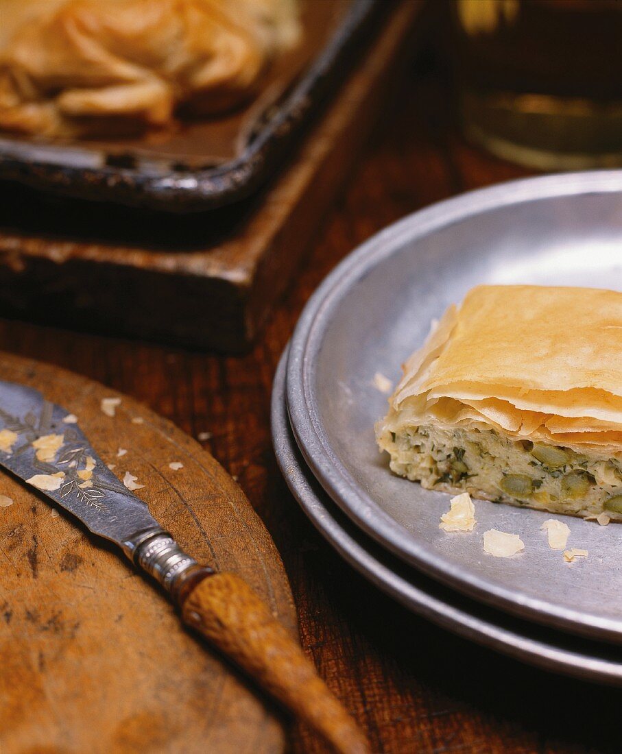 A Piece of Leek and Asparagus Strudel on a Metal Plate; Knife