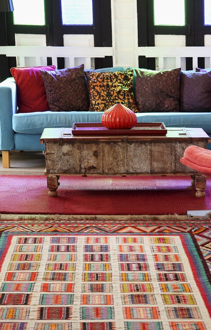 Colourful rug in front of onion-shaped vase on vintage coffee table and blue sofa with patterned cushions
