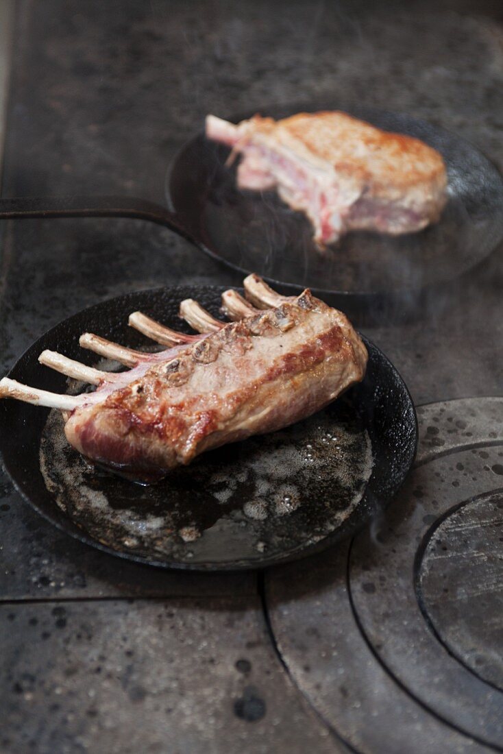 A rack of lamb and a veal chop being fried in a pan