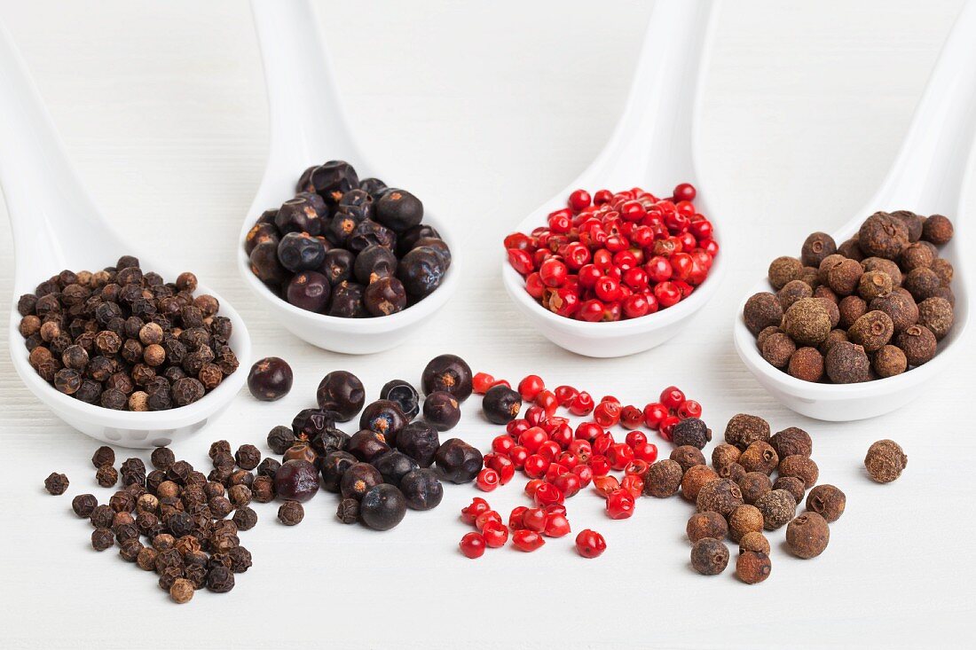 Allspice berries, pink pepper, juniper berries and black peppercorns on spoons