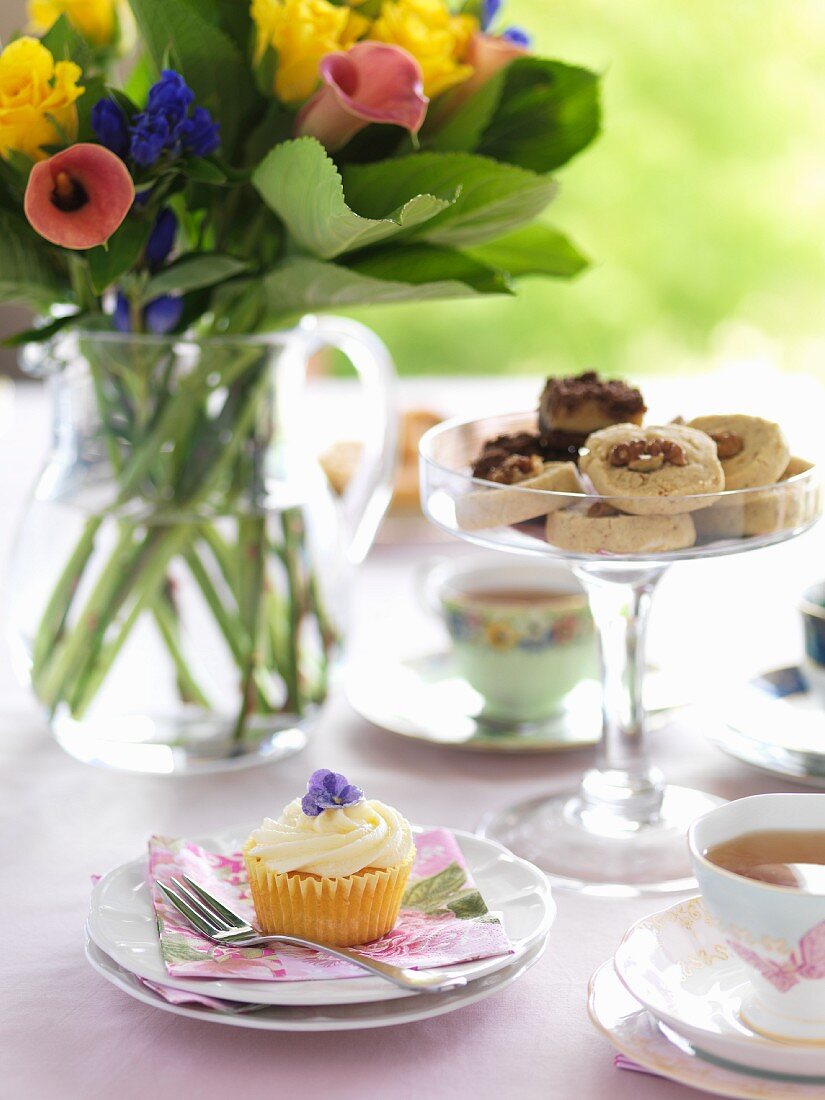 A table laid with a bunch of flowers, cupcakes and tea
