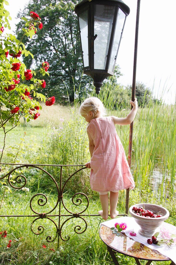 Little blond girl balancing on the railing of a garden pavilion