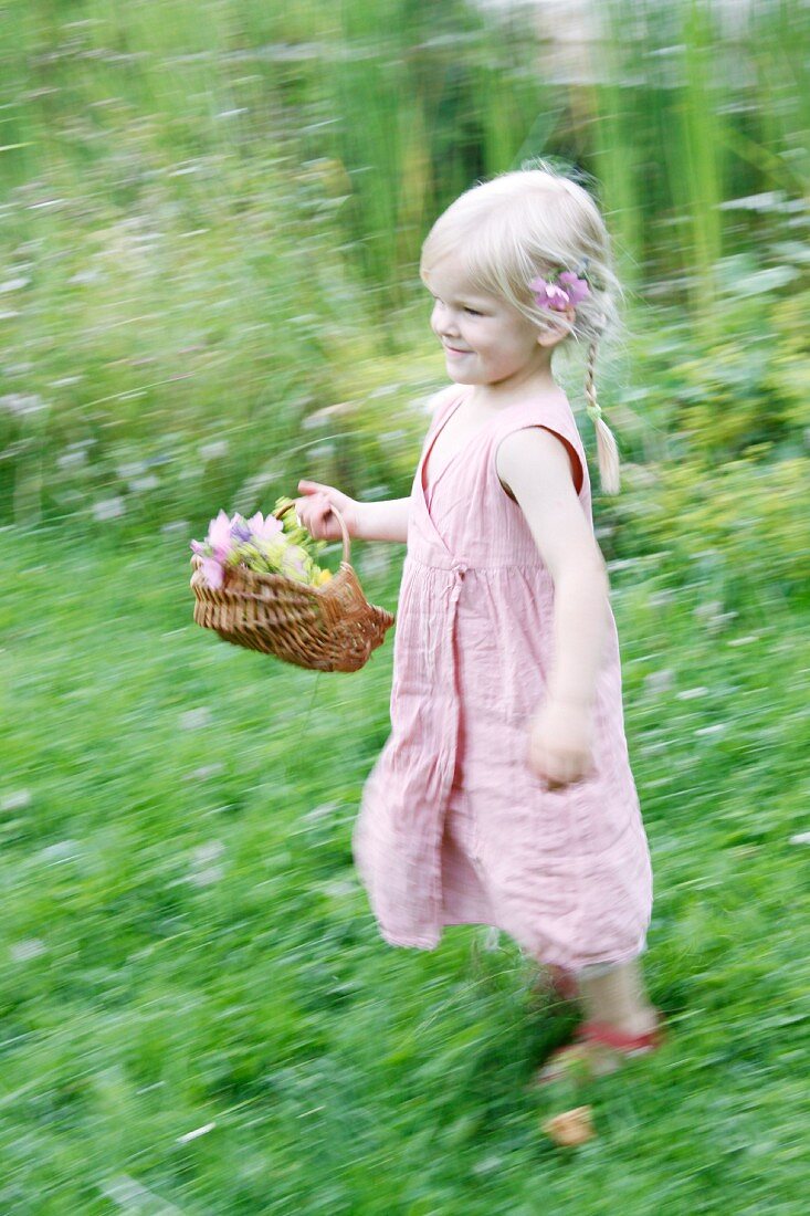 Blondes Mädchen läuft mit Blumenkorb durch den Garten
