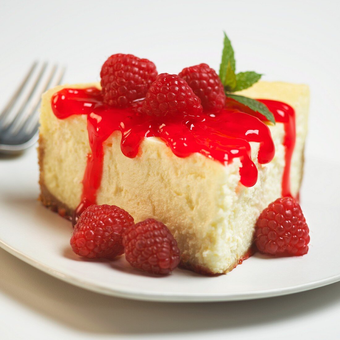 Slice of Cheesecake with Raspberry Sauce; On a White Plate; Close Up