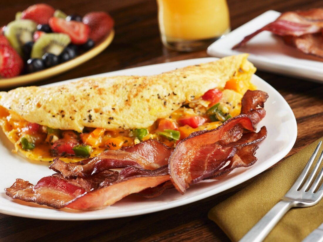 Strips of Smoked Bacon with a Veggie Omelet on a White Dish' Fruit Salad and Orange Juice