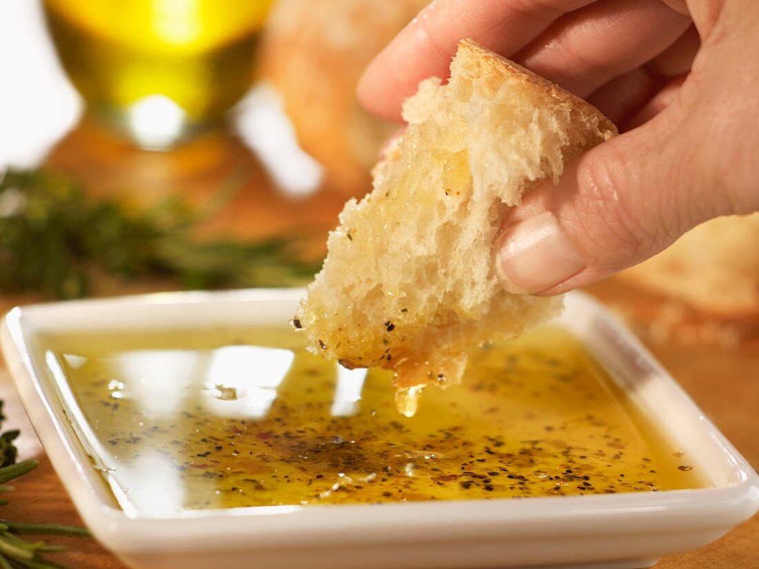 Hand dippt Brotstück in Olivenöl