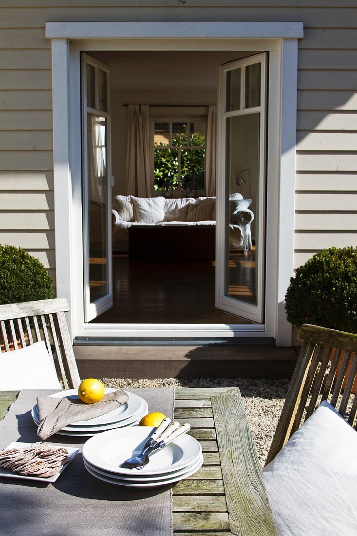 Plates and lemons on terrace table in front of open terrace doors of wooden house with view into interior