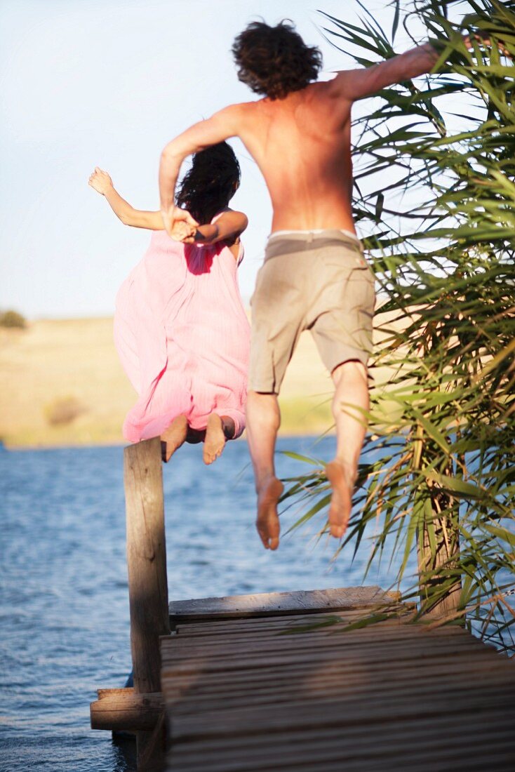 Couple jumping off dock into lake