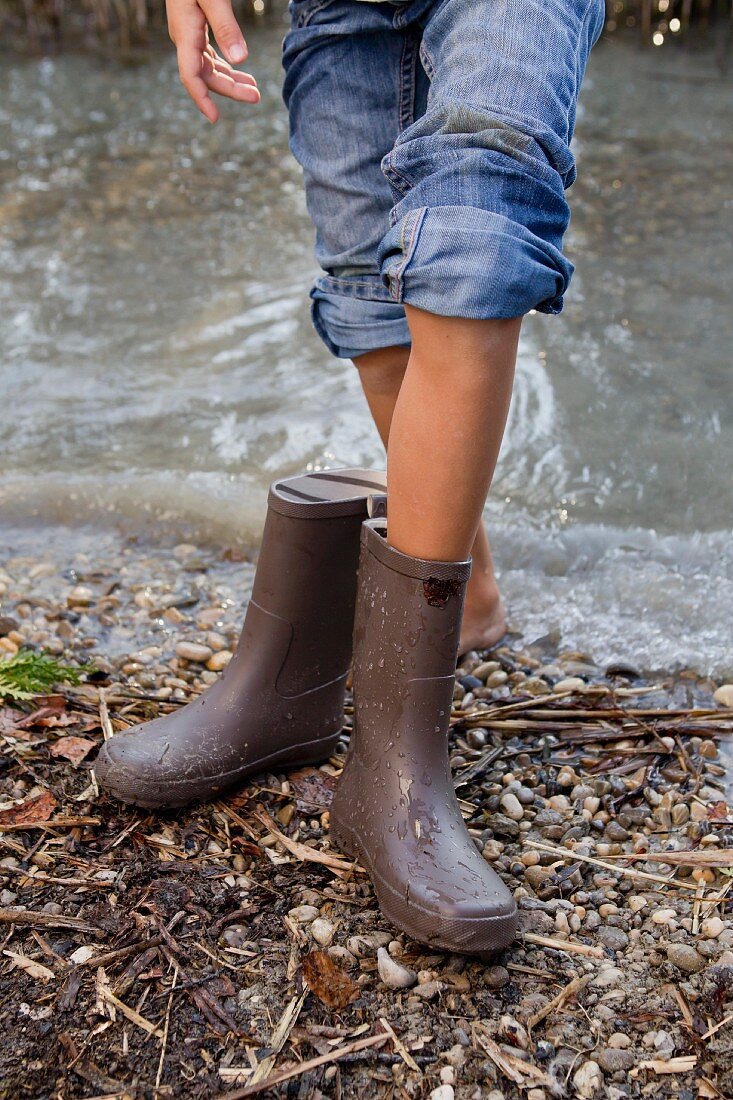 Girl taking off rain boots by pond